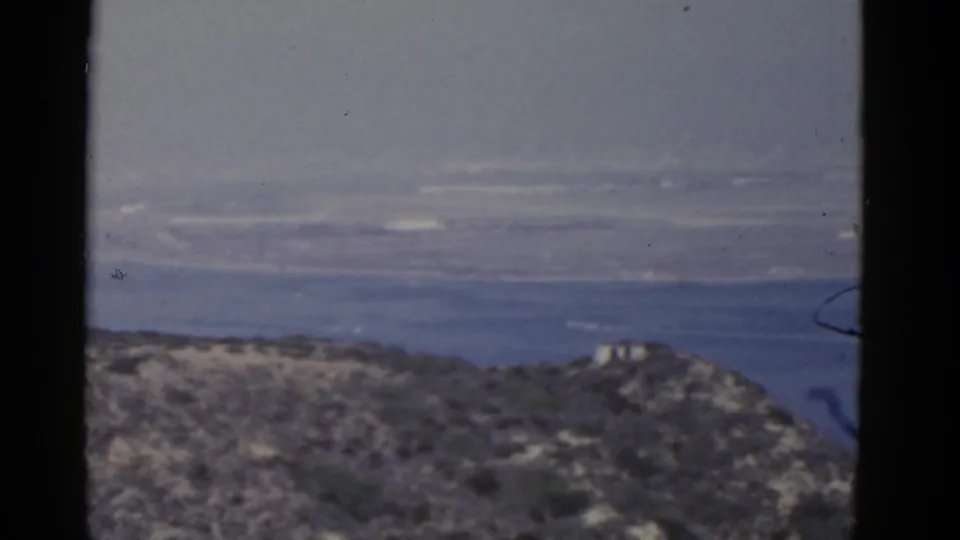 1952 California home-movie frame showing scrubby coastal hills and a distant blue ocean horizon through soft 8mm grain.