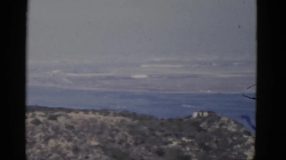 1952 California coastal view with a hazy sea horizon, low scrub-covered hills, and visible 8mm frame edges.