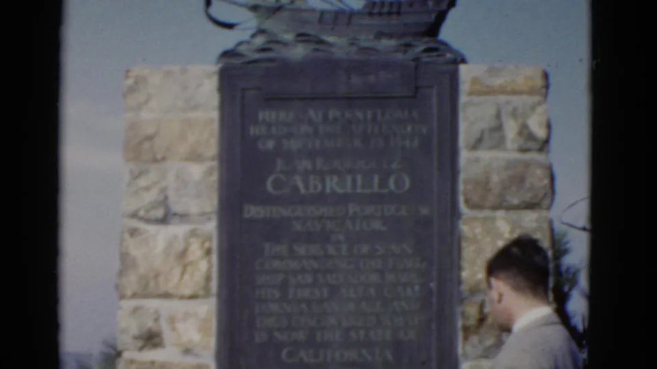 A man in a light-colored suit passes in front of the Cabrillo monument during a 1952 California home-movie shot.