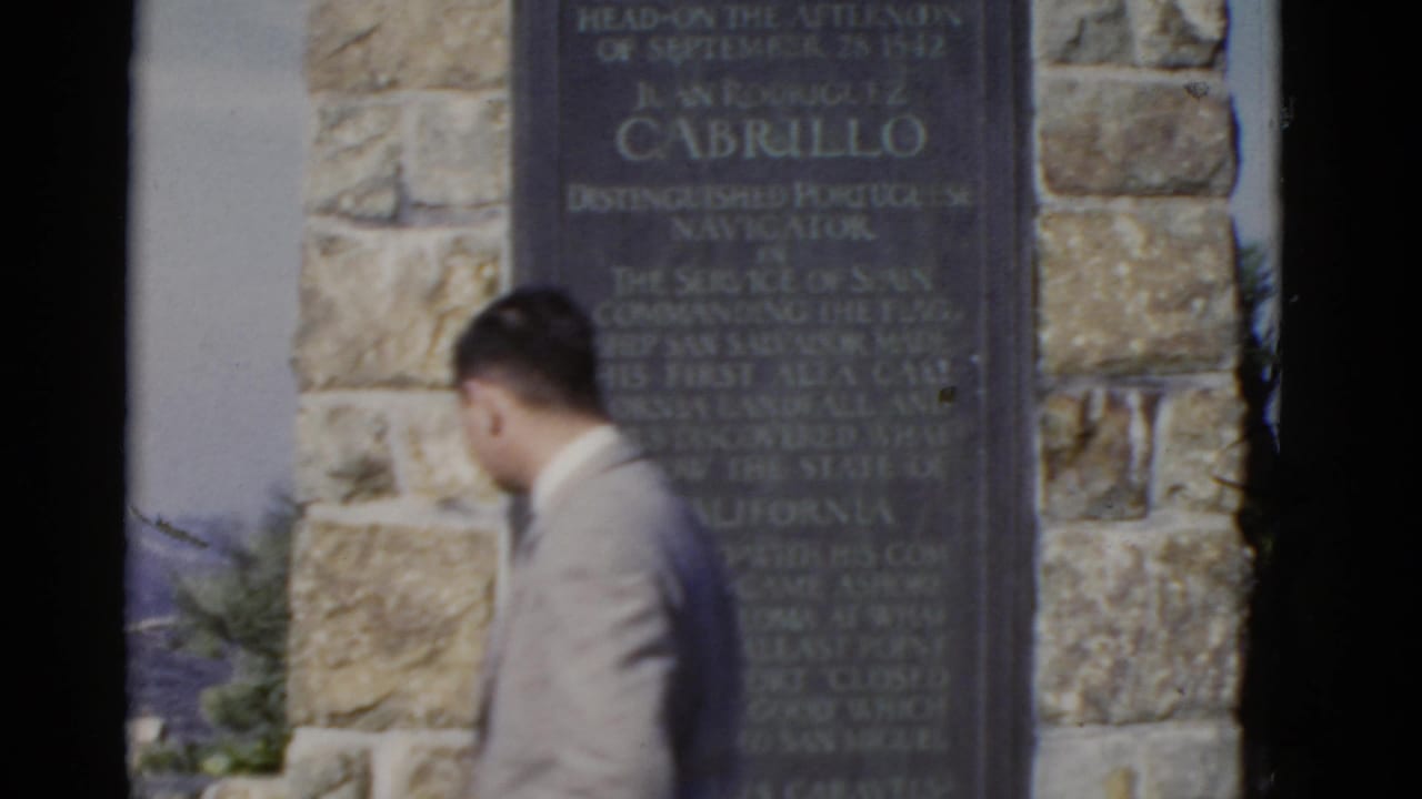 Suited man passes a black monument plaque set in a stone wall.