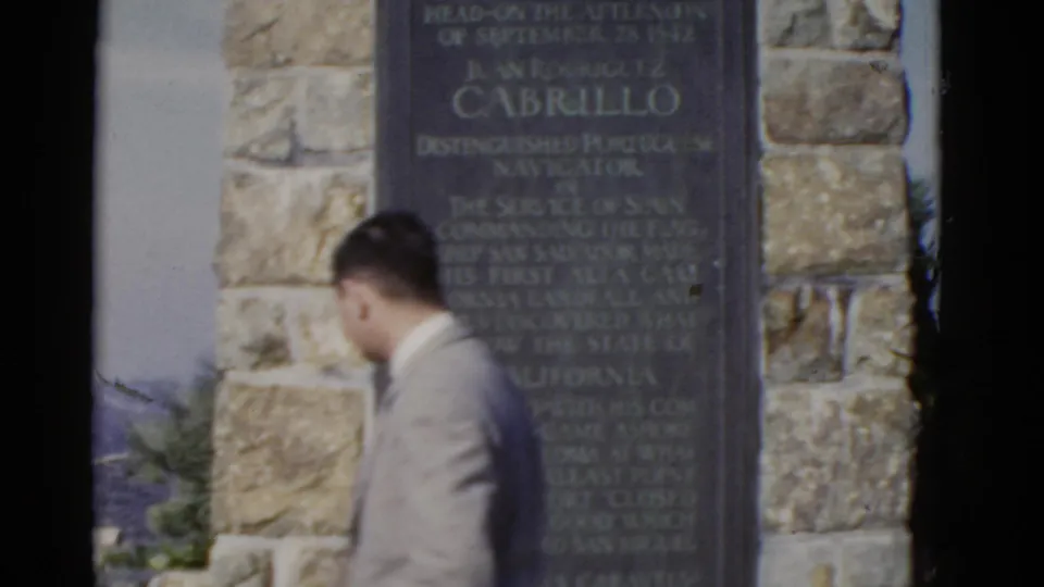 A suited adult walks past the Cabrillo National Monument plaque in a 1952 California home-movie frame.