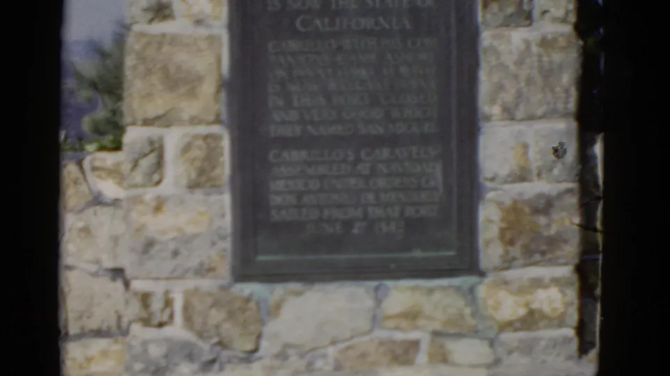 The Cabrillo National Monument plaque fills the frame within rough stone masonry in 1952 California footage.
