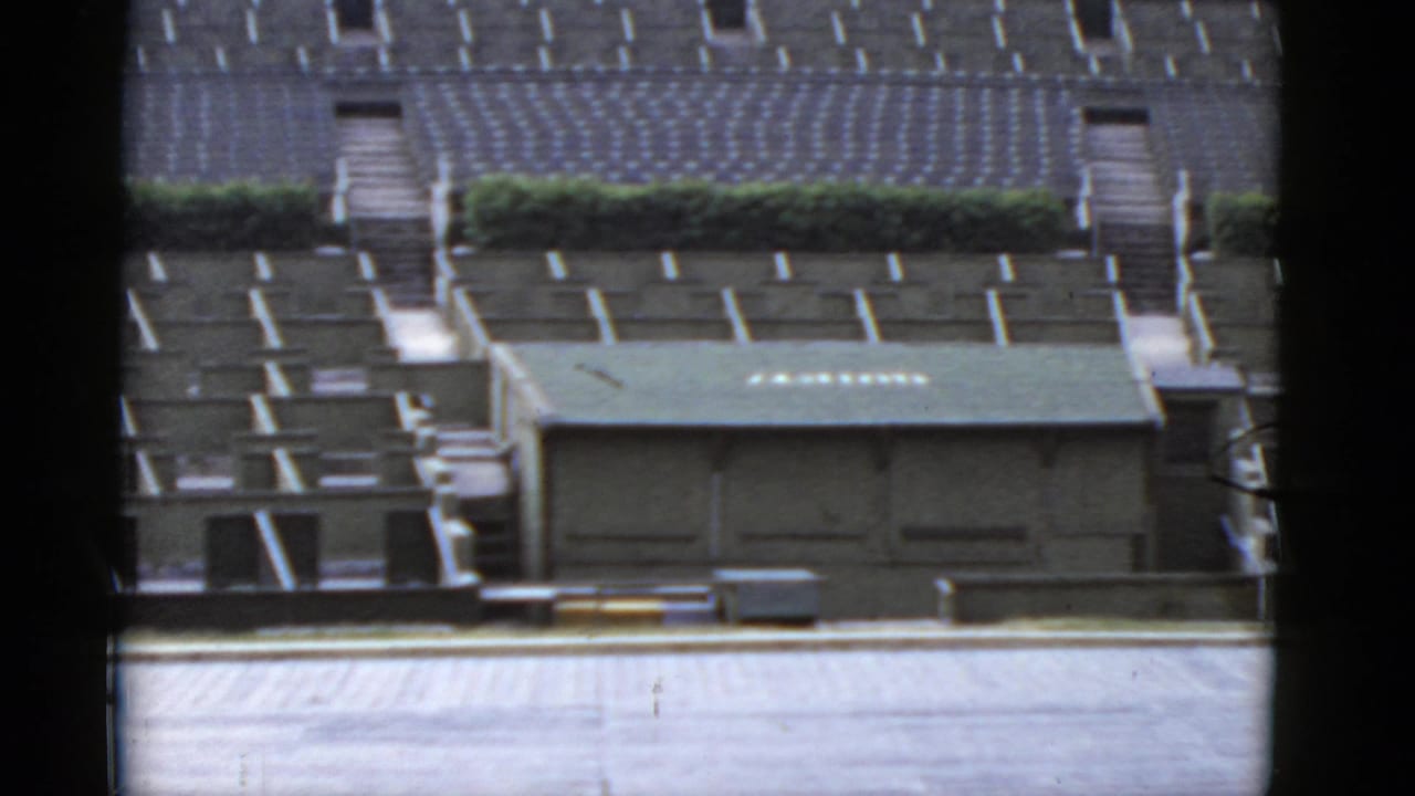 Empty outdoor bleachers and a small roofed structure seen through dark film-frame edges.