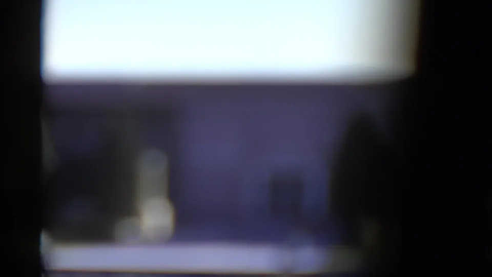 Soft 8mm transitional frame with blurred building shapes, dark vertical foreground edges, and bright sky or facade area.