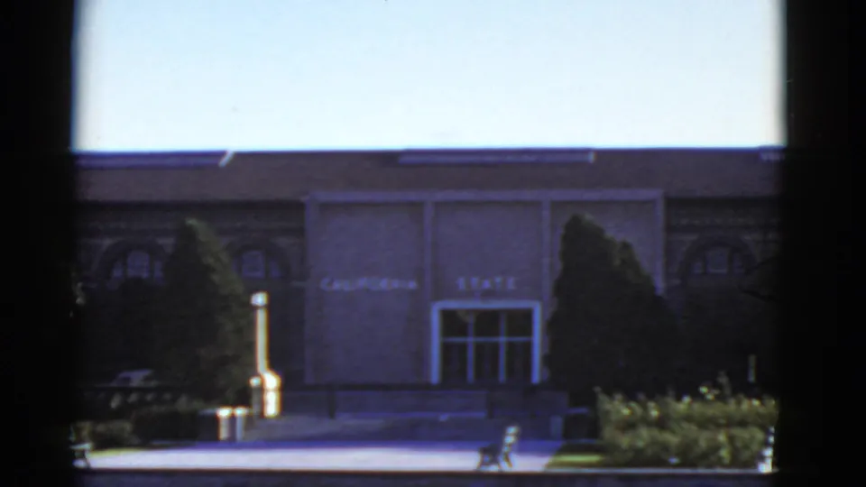 1952 California 8mm frame showing an institutional building entrance marked "CALIFORNIA STATE" with landscaping and trees.