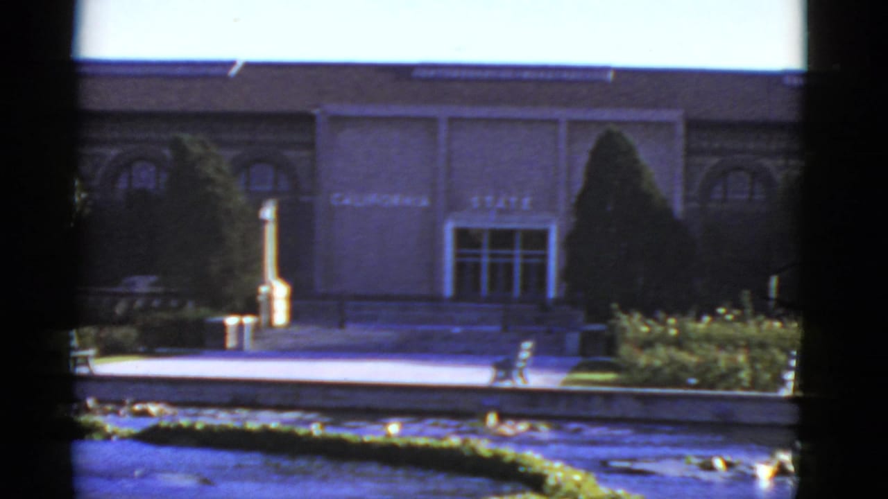 1952 California home-movie view of a state building facade, entrance steps, pond, lily pads, hedge, and benches.