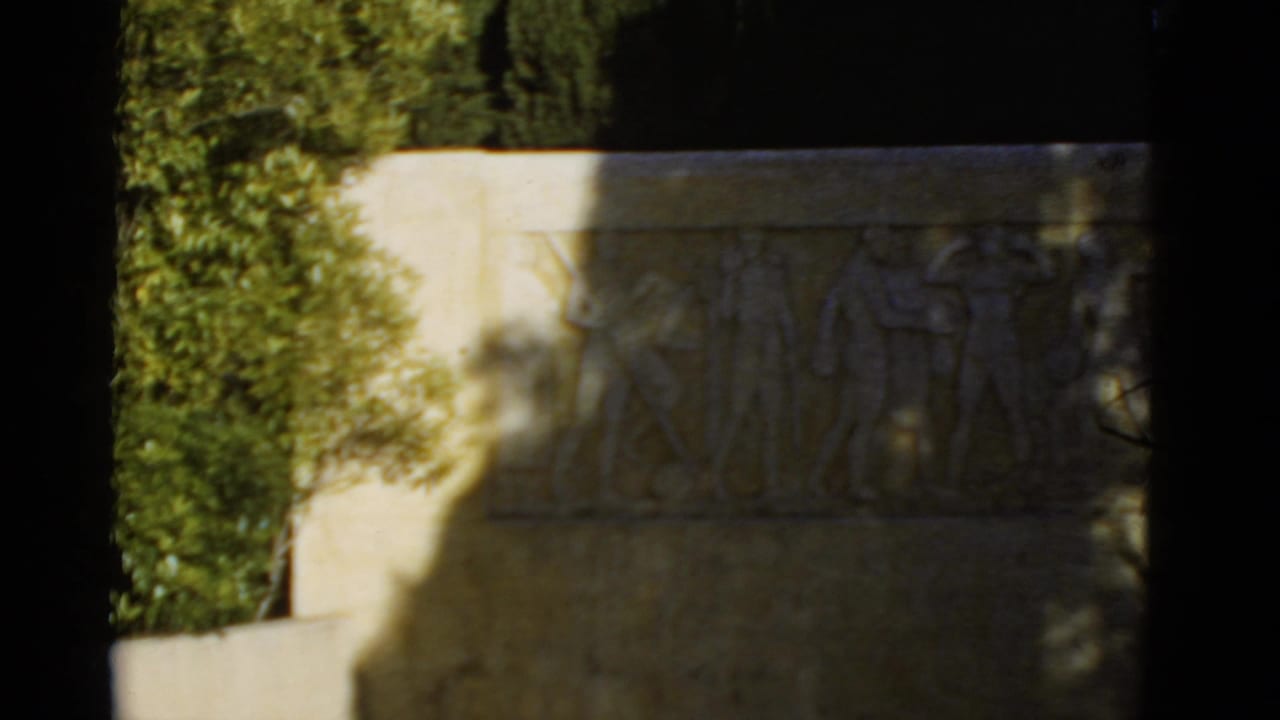 Pale stone relief plaque with carved athletic figures partly shaded by trees.