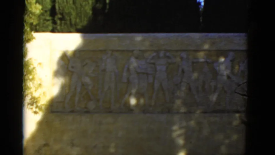 1952 California 8mm view of the athletic relief plaque, showing carved figures, pale masonry, and heavy shadow along the frame edge.