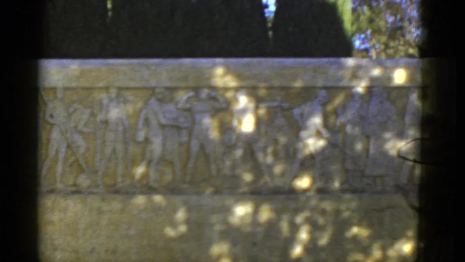 Final 1952 California frame showing the athletic relief plaque under moving tree shadows, with dark greenery rising behind the monument.