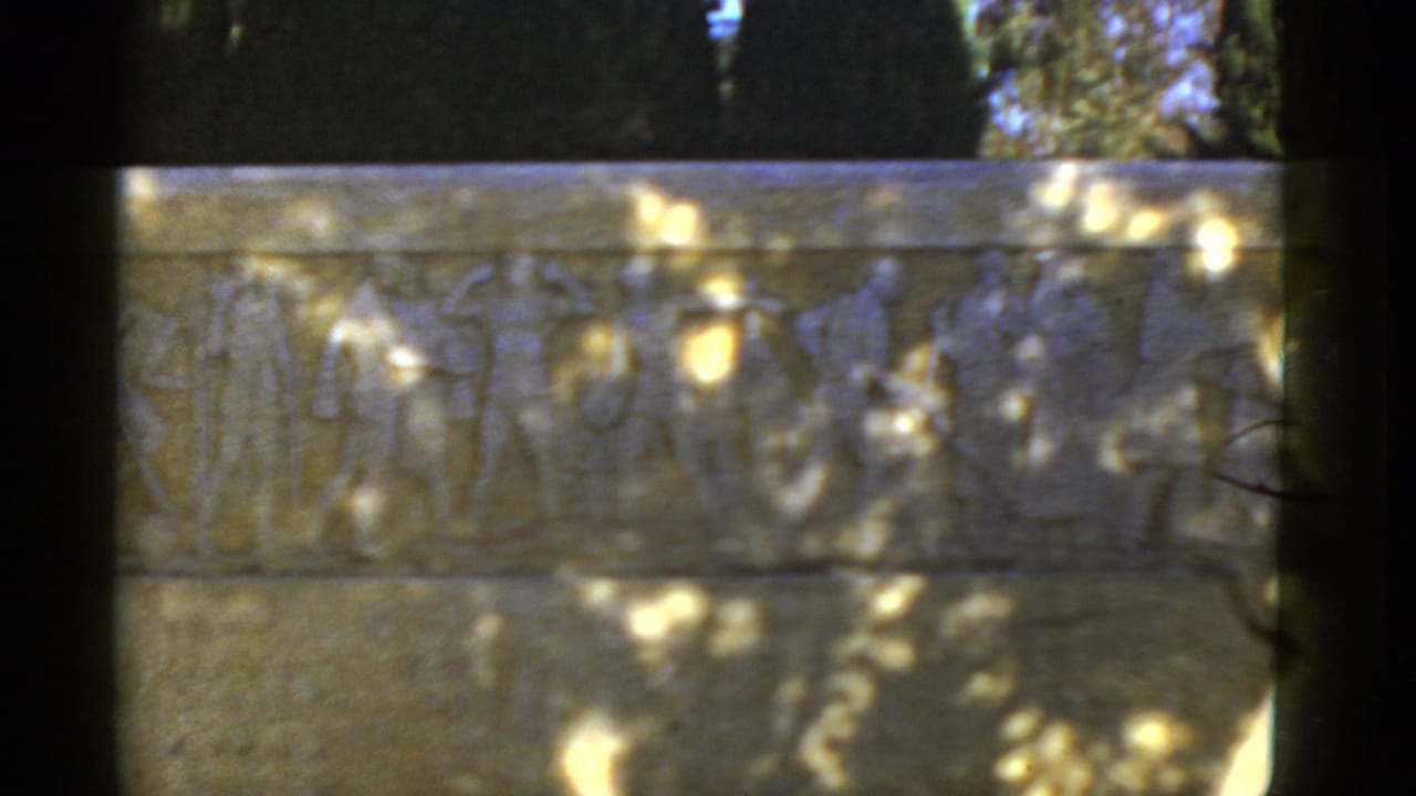 1952 California 8mm frame showing an outdoor stone relief with robed figures, dappled sunlight, and dark film-frame borders.