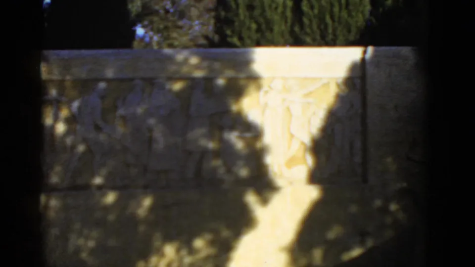 Final 1952 California 8mm frame showing a classical-style stone relief, tree shadows, and a bright patch of sunlight across the carving.