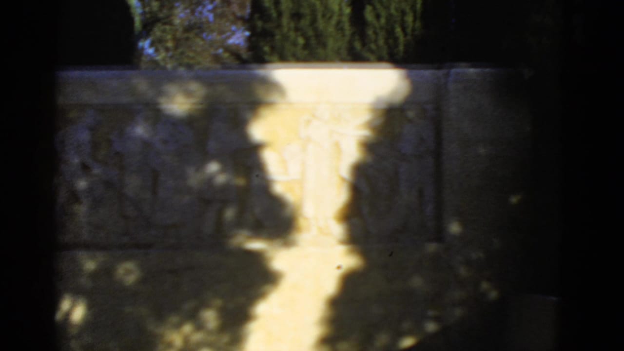 Soft, shadowed view of a stone relief or wall beside a bright walkway.