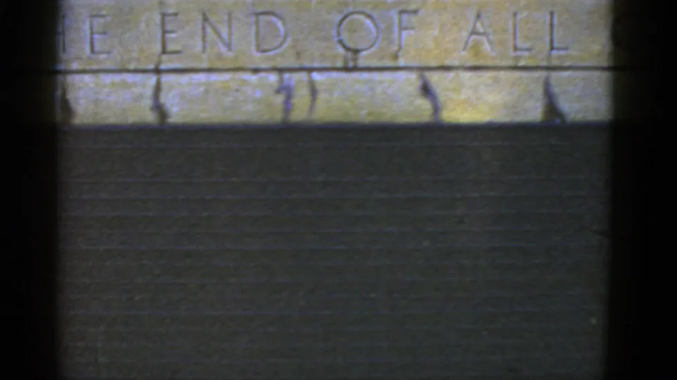 The 8mm frame holds on a weathered stone inscription, partly legible as “THE END OF ALL,” above a dark wall plane.