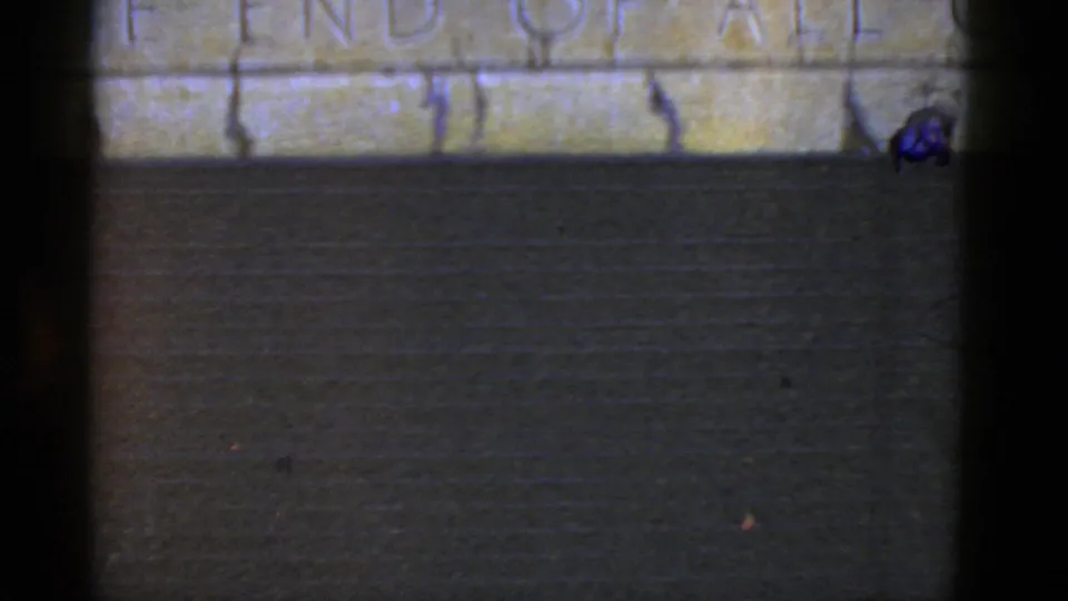 Final 1952 California frame showing the lower part of a carved stone inscription above a dark wall, with film-edge shadowing.