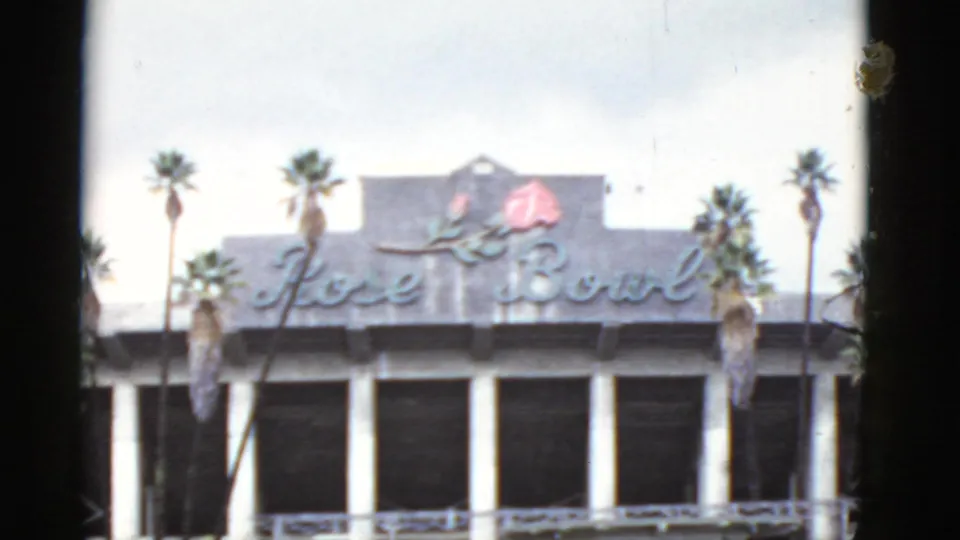 1952 California 8mm frame showing Rose Bowl script signage, a red rose emblem, palm trees, white columns, and dark windows.