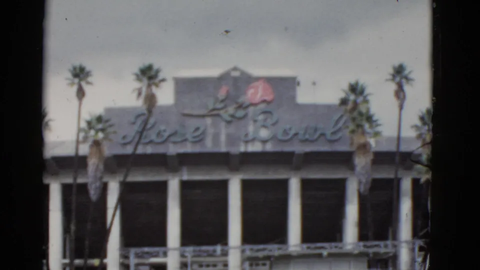 Soft-focus 1952 8mm frame showing the Rose Bowl sign, rose emblem, palm trees, columns, and upper building details.