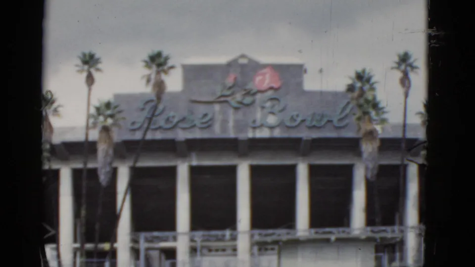 End frame of the California Rose Bowl sign exterior, with palm trees, white columns, dark windows, and visible 8mm film edges.