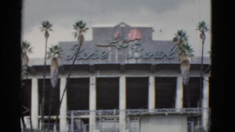 1952 California home-movie view of the Rose Bowl exterior with its cursive sign, rose emblem, white columns, and palms.
