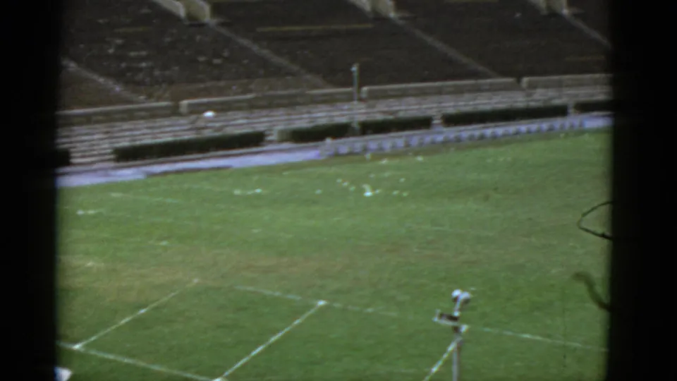 High-angle 1952 California view of an empty football field, showing worn grass, white field markings, and vacant stadium seating.