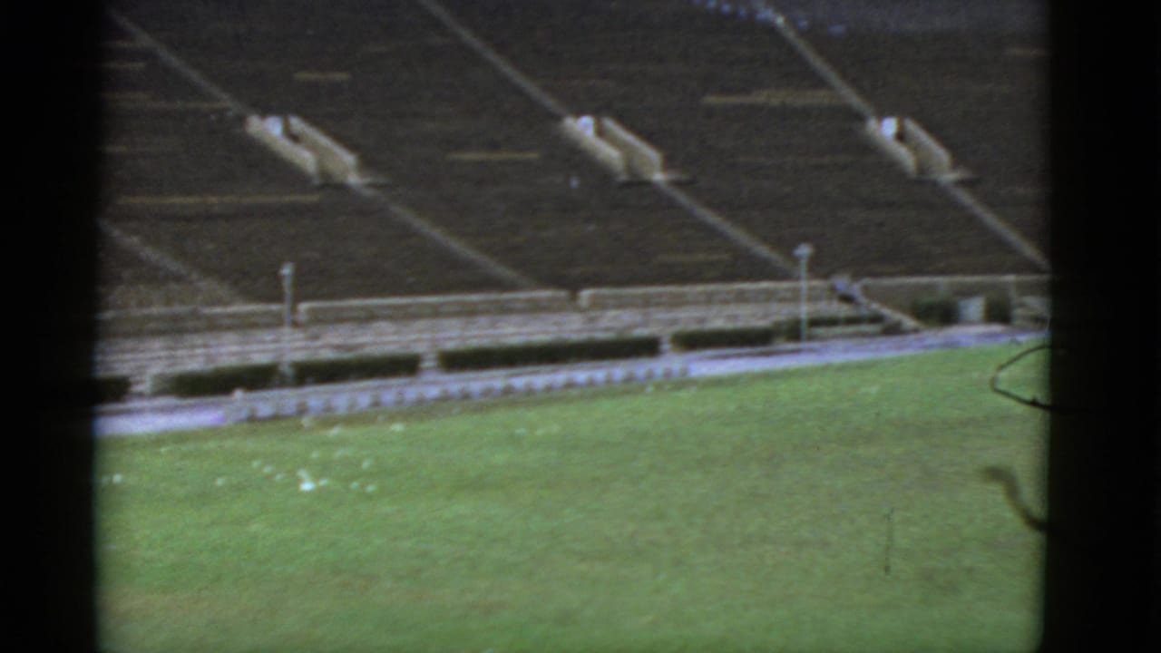1952 California home-movie frame showing an empty football stadium from high above, with green turf and vacant concrete stands.