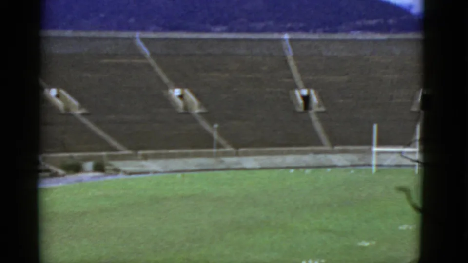 1952 California home-movie view of an empty stadium, with concrete stands, a green field, white goalposts, and distant hills.
