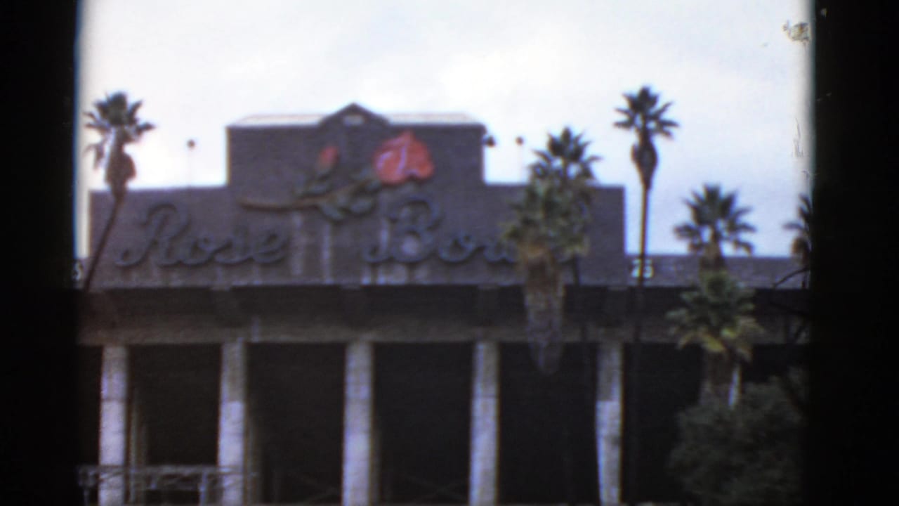 1952 California home-movie frame showing a building facade with a visible Rose Bowl sign, palm trees, and soft exposure.
