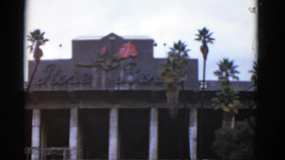 1952 California home-movie frame showing a building facade with a visible Rose Bowl sign, palm trees, and soft exposure.