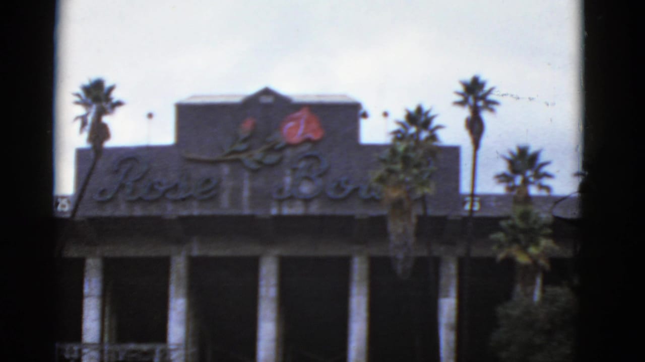 Rose Bowl facade with cursive sign, red rose emblem, palm trees, and dark window framing.