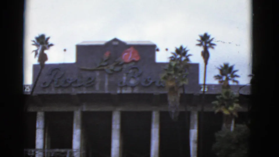 1952 California 8mm view of the Rose Bowl building facade with signage, red rose emblem, white columns, and palm trees.