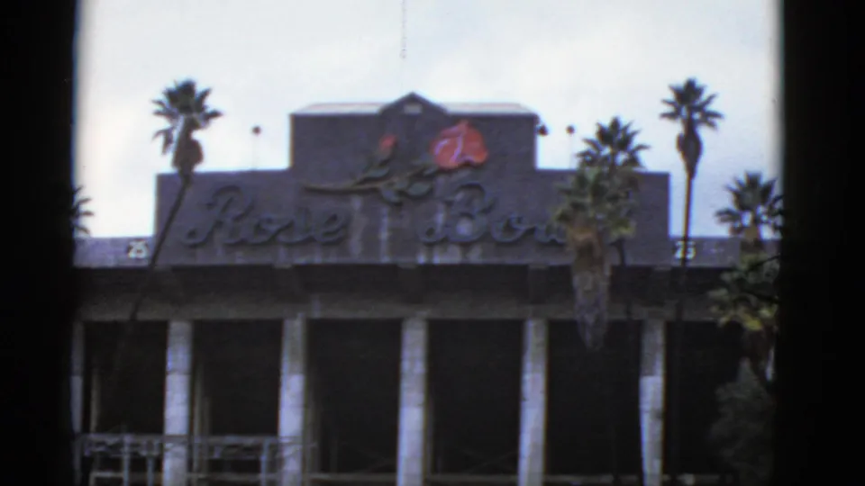 1952 California 8mm frame showing the Rose Bowl building sign, red rose emblem, columns, palms, and partial lower railings.
