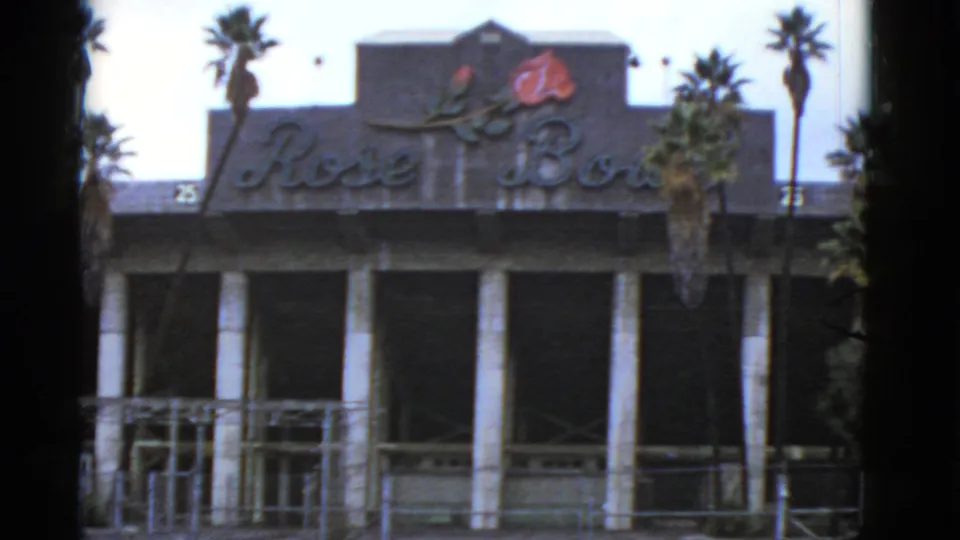 Final 1952 California frame of the Rose Bowl exterior, showing the sign, emblem, palms, white columns, and foreground framing.