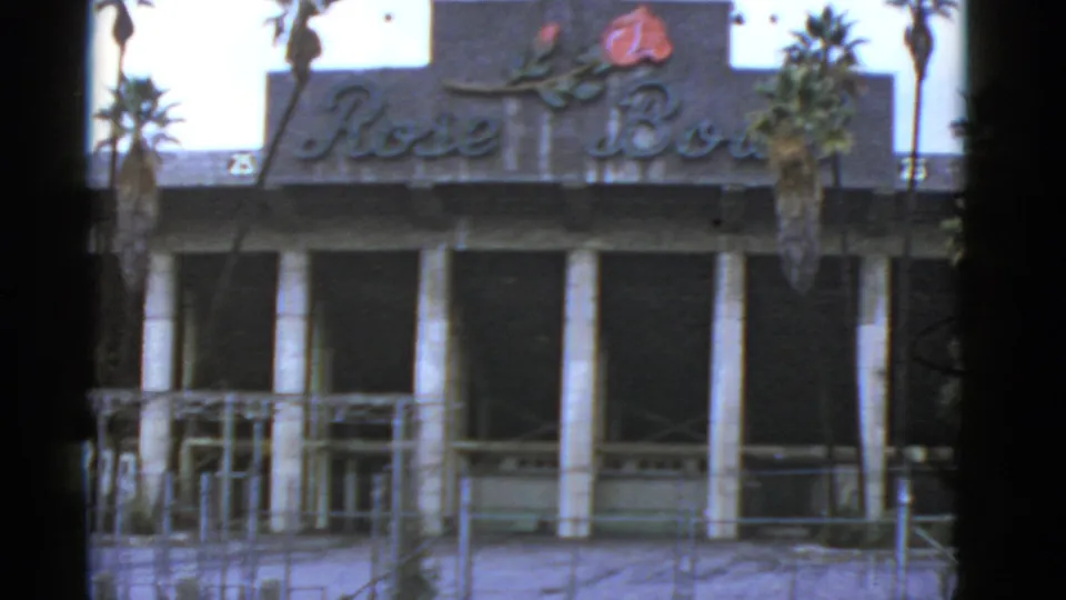 1952 California 8mm frame showing a faded Rose Bowl sign, palm trees, columns, dark windows, and a fenced worn exterior.