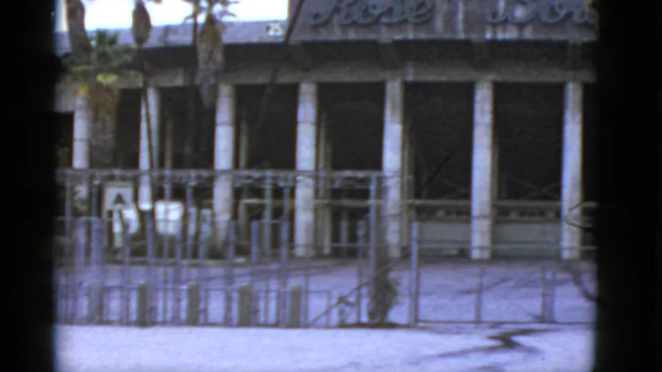 1952 California 8mm frame showing the lower Rose Bowl facade area with palm trunks, partial lettering, fencing, scaffolding, and dark openings.