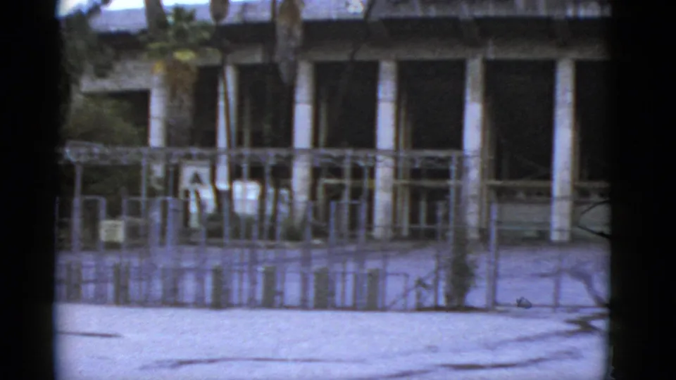 1952 California frame of the closed-looking Rose Bowl exterior, showing columns, palm trunks, scaffolding, fence lines, and shadowed window bays.