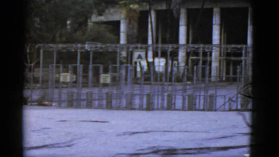 1952 California frame with metal rail fencing, a gray gate area, trees, and a modern columned building beyond.