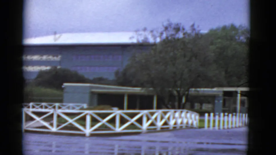 1952 California frame with white fencing, trees, paved ground, and low structures at an outdoor entertainment site.