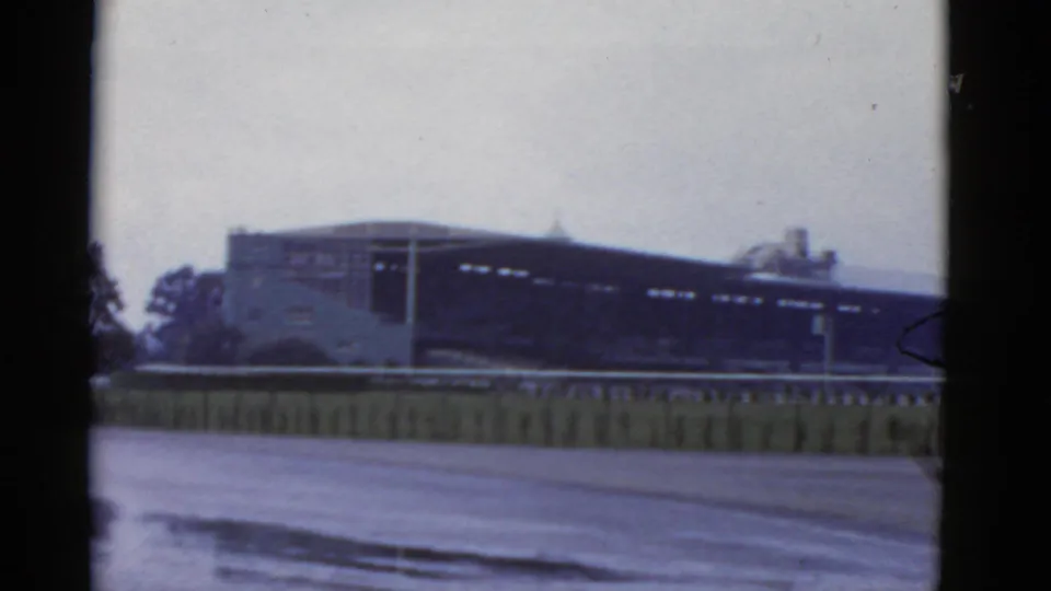 1952 California 8mm frame showing a long, low building beyond an empty paved area and a low fence or barrier.