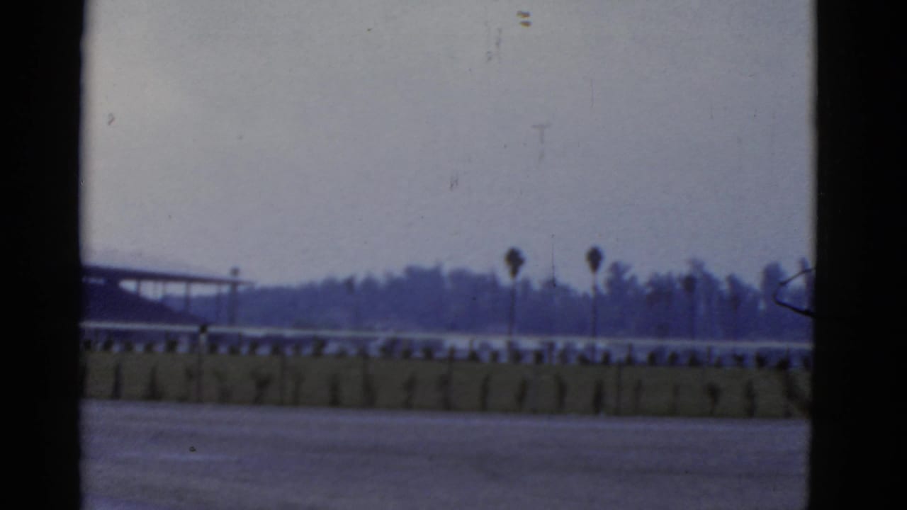 1952 California 8mm frame showing a distant road or waterfront scene with palm silhouettes and a low barrier.