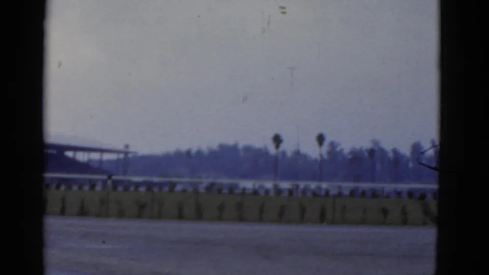 1952 California 8mm frame showing a distant road or waterfront scene with palm silhouettes and a low barrier.