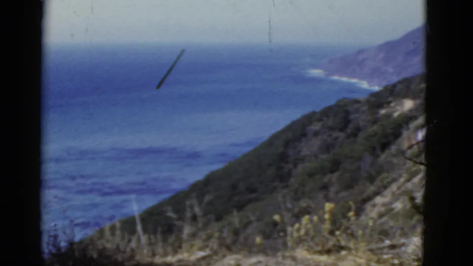 The final frame shows the California coastal hillside, blue Pacific water, distant shore, dry plants, and visible 8mm film marks.