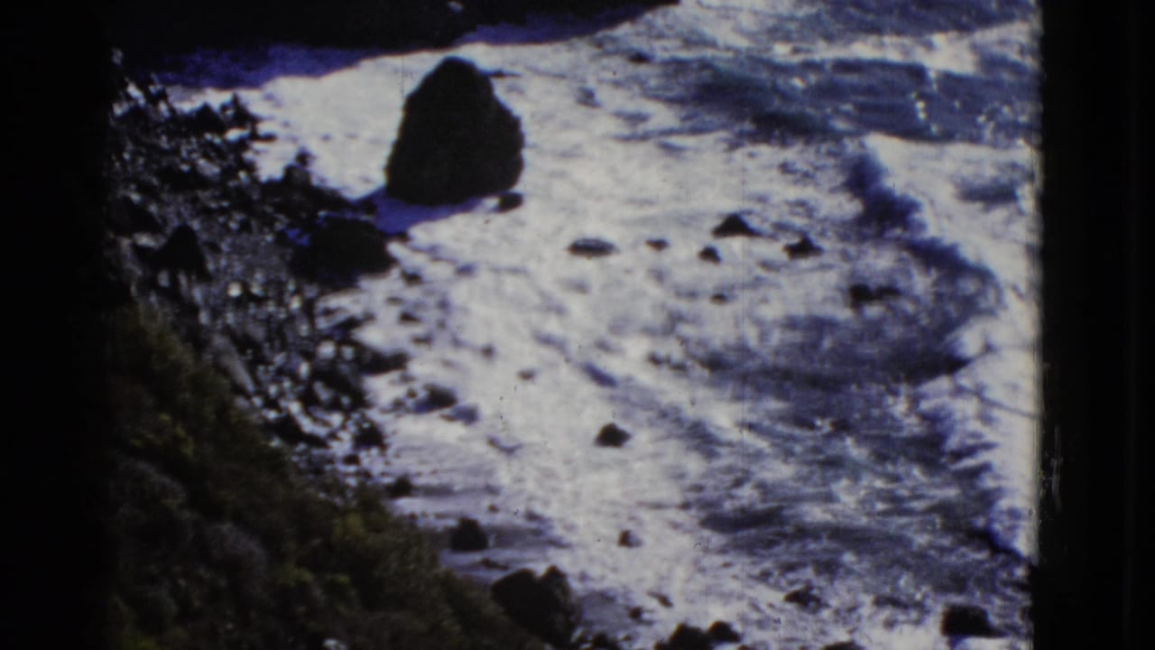 Waves spread white foam across a rocky shore with a large sea stack.