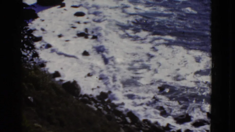 1952 8mm San Francisco ocean footage shows foamy wave patterns spreading across a rocky coastal edge with no people visible.