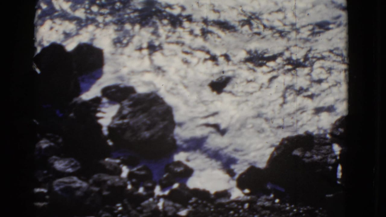 1952 San Francisco home-movie frame showing white ocean water breaking against dark coastal boulders from above.