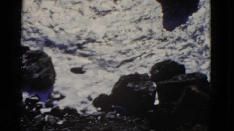 Grainy 1952 San Francisco shoreline frame with white water flowing between dark coastal rocks.