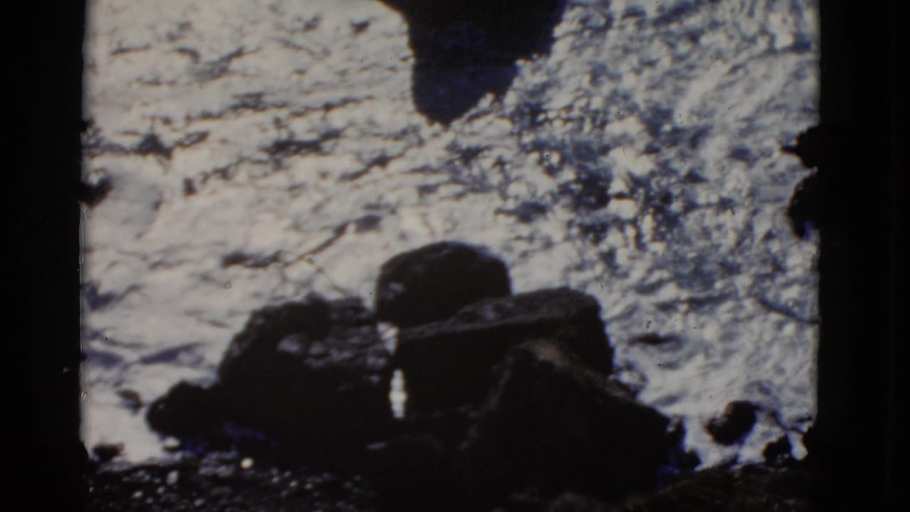 1952 San Francisco home-movie frame showing dark shoreline rocks with foamy surf and a cropped film-frame edge.