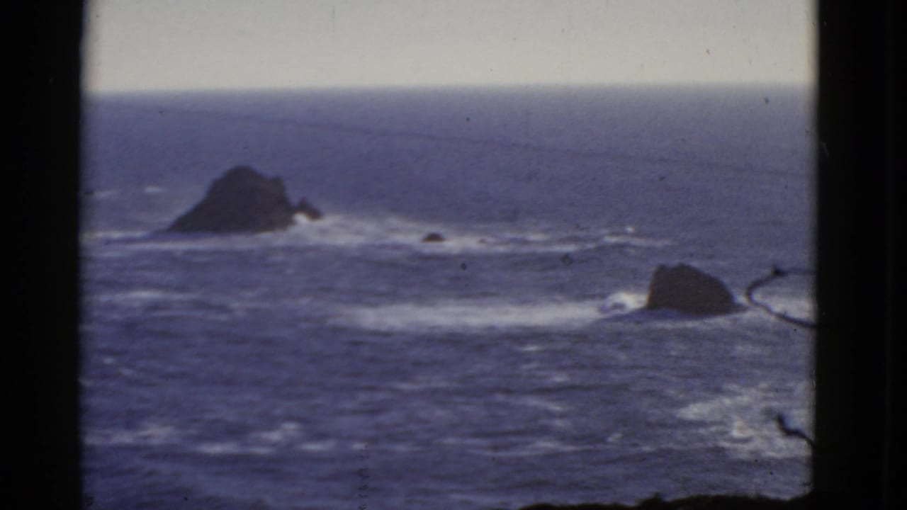 1952 8mm San Francisco coastal view with blue water, white surf, dark rocks, and heavy black frame edges.
