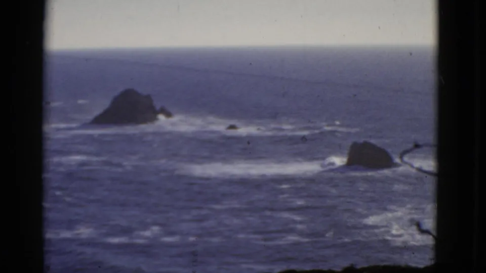 1952 8mm San Francisco coastal view with blue water, white surf, dark rocks, and heavy black frame edges.
