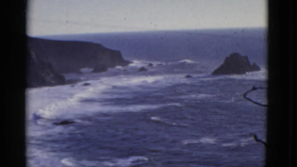 Final 1952 San Francisco coastal frame shows a wider view of headland, offshore rocks, white surf bands, and dark framing edges.