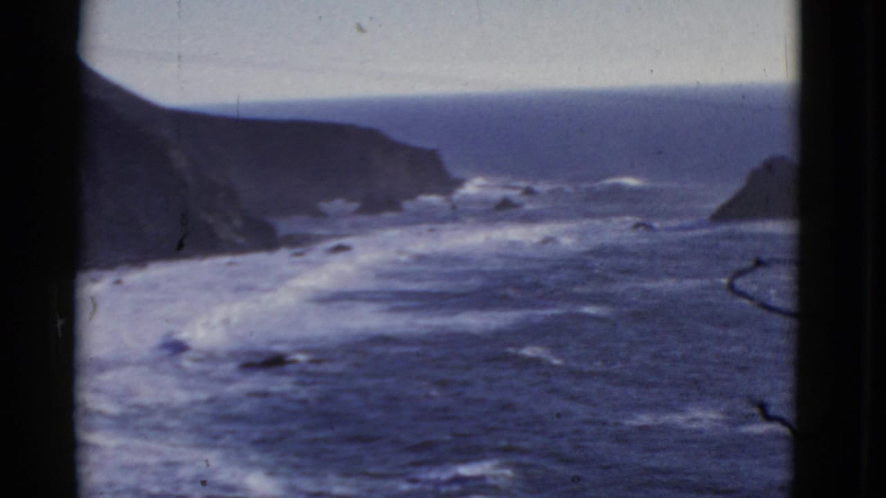 Ocean waves roll toward dark cliffs along a rugged coastline.