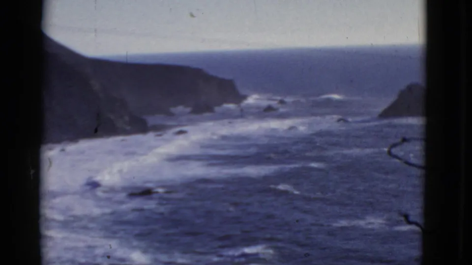 1952 8mm home-movie view of surf moving toward steep coastal cliffs near San Francisco, with dark film edges visible.